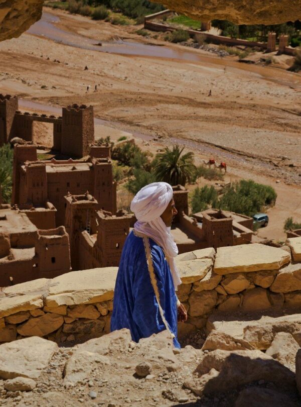 a woman in a blue dress standing in front of a desert village
